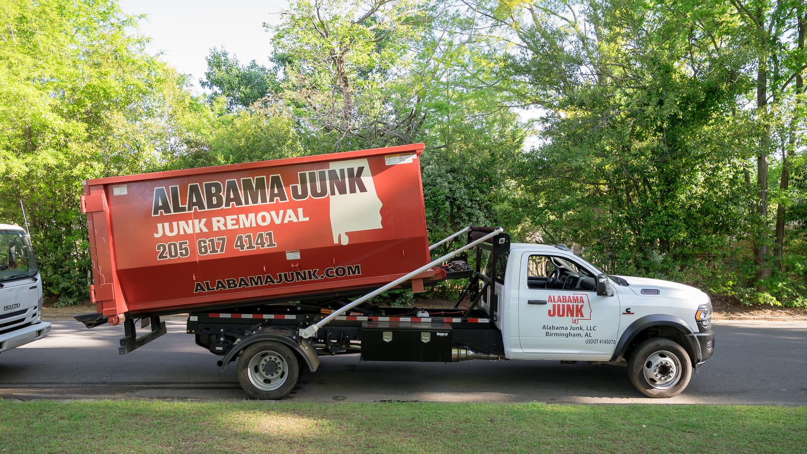 Alabama Junk hook-lift truck with the red container parked on a lawn-side street