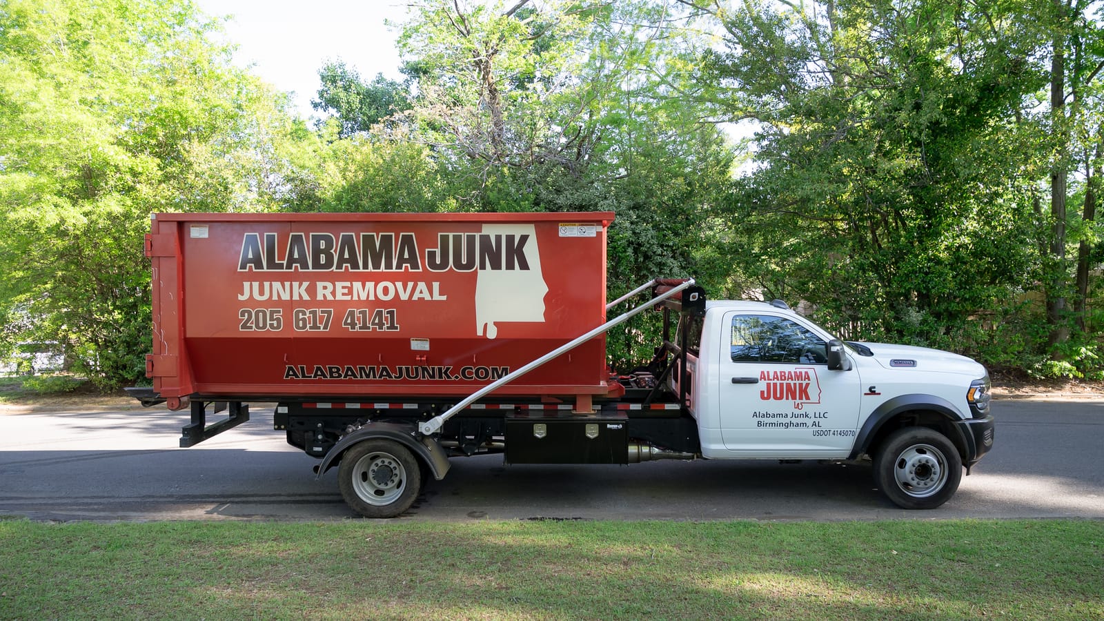 Alabama Junk hook-lift truck with the red container on a tree-lined street