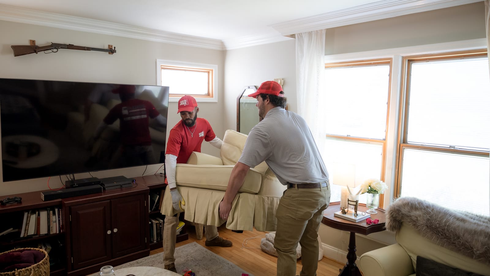 Two Alabama Junk Removal crew members carrying an upholstered armchair out of a Birmingham living room